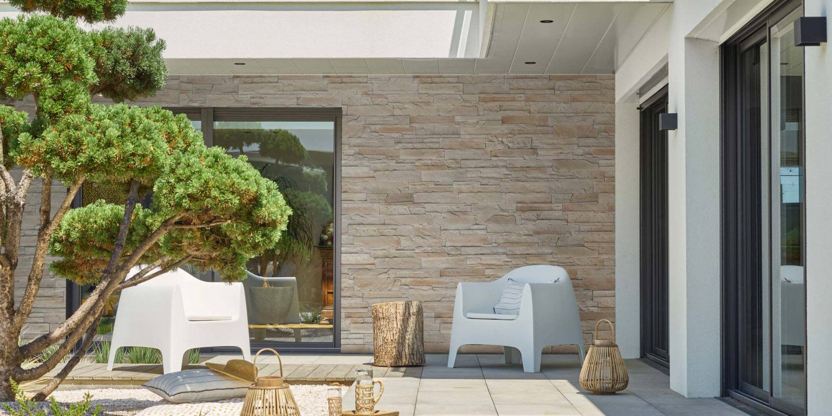 Maison moderne blanche en parement Portland ton naturel, terrasse en dalle de béton et mobilier moderne.