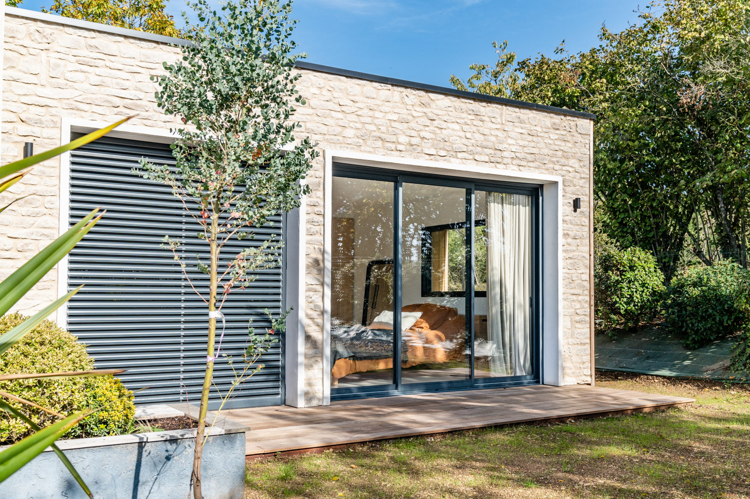 Façade d'une maison moderne revêtit de parement Causse ton naturel et porte vitrée donnant sur l'extérieur