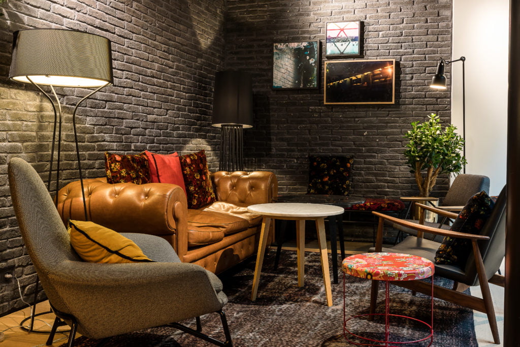 Small lounge in the LAZ' Hotel, wall clad in black-tone brickwork with leather and fabric armchairs.