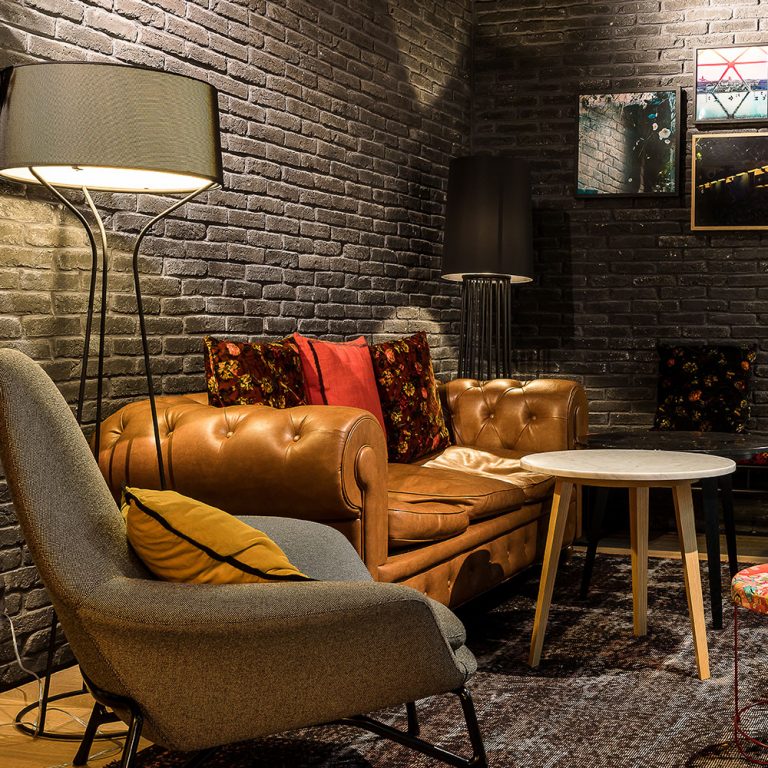 Petit salon du LAZ' Hotel, mur recouvert de parement Brique ton black avec fauteuils en cuir et tissus.